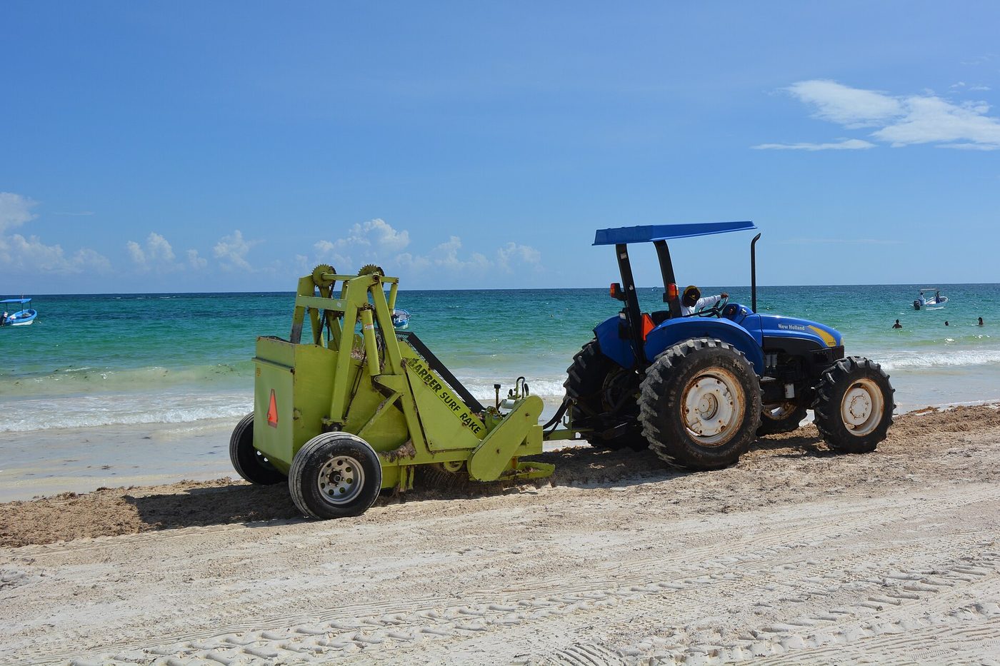 Tractor con rastrillo de limpieza retirando algas en una playa tropical